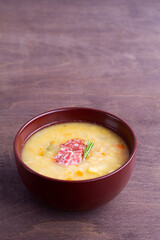 pea soup with ham, carrots and potatoes on a rustic wooden background. Classic Dutch pea soup erwtensoep, snert with bacon in the brown bowl on the table. vertical. copy space