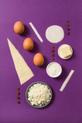 The ingredients for homemade cheesecake: eggs, sugar, flour, cottage cheese on purple background. Home cooking, baking concept. Top view.
