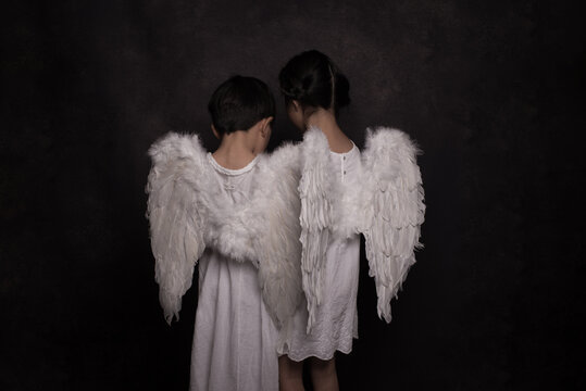 Rear view of girl and boy in white angel costume standing indoors