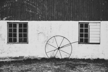 Old farm barn wall with rustic wheel. Building exterior. Windows and wood.  