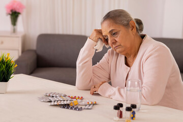 Sick old woman sitting with medicines kept on centre table