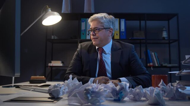 Businessman crumpled paper. Stressful state of the man who looks at the paper in his hand and does not like it and crumples it.  There is a lot of crumpled paper in front of it.