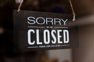 Sorry we are closed sign board hanging on glass door of cafe or store