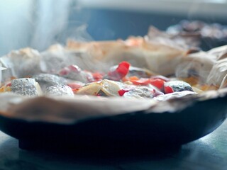 A frying pan just removed from the oven with baked potatoes with vegetables and chum fish, using baking paper. Hot steam comes from food.
