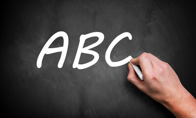 The teacher's hand writes A, B, C on the black board with white chalk