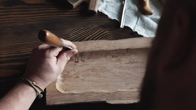 view from above. a woodcarver processes a oak wood board with a chisel. woodworking process with hand tools in a carpentry workshop. wood carving concept
