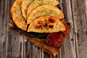 Hot homemade chebureki pies with minced meat, onion and pepper on plate, wooden background