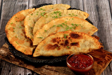 Hot homemade chebureki pies with minced meat, onion and pepper on plate, wooden background