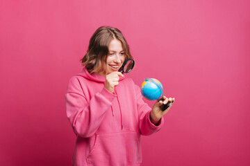 Young cheerful woman looking at globe trough magnifying glass for next travel destination.