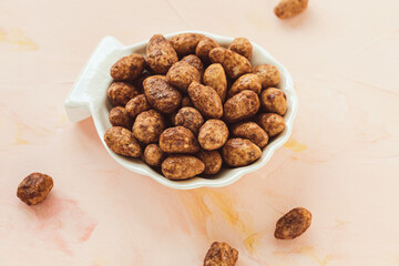 Candied or sugared almond with honey and cinnamon in a small porcelain plate on pink background. Traditional Christmas sweets for holidays. Copy space