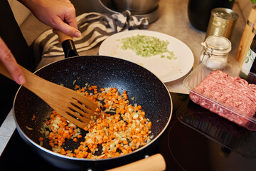 Woman cooking bolognese sauce in pan on induction stove in the kitchen