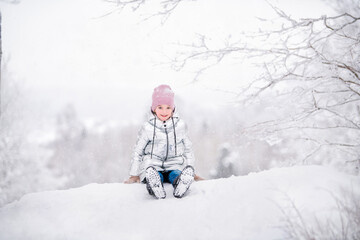 Fototapeta na wymiar little girl sitting on snow in park in winter