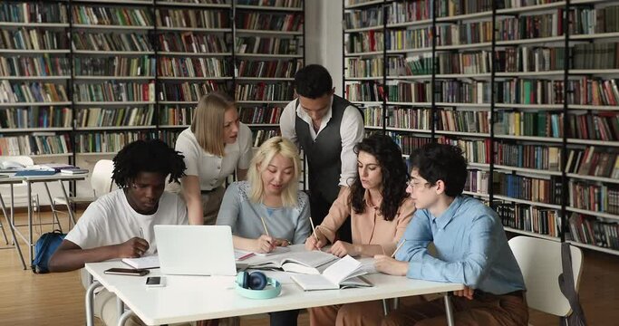 Education using laptop, gen Z, modern tech usage, teamwork concept. Six multiracial students gather in university library preparing fox exams, studying, discuss topics, work together on creative task