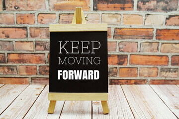 Keep Moving Forward typography text on the blackboard set on wooden floor and brick background