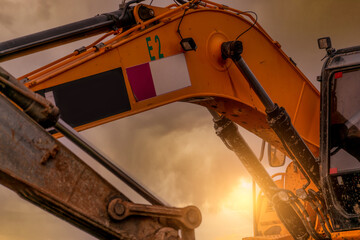 Closeup hydraulic piston arm of dirty backhoe at construction site. Yellow excavator parked at construction site against sunset sky. Digger machine. Hydraulic machinery. Excavator for rent business.