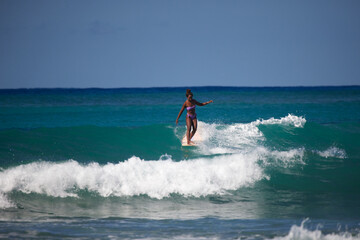 Charming curly African-American dark-skinned young woman, professional surfer ride a surfboard in...
