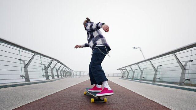 Close-up of a guys legs performing complex tricks on a skateboard on the city bridge. Jump and flip. Back view