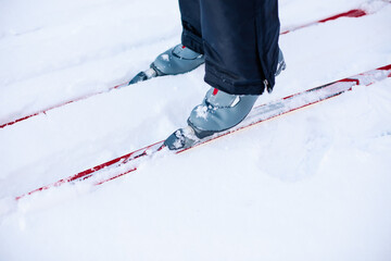 Close-up of skis and grey ski boots. Man skiing on winter snow on clear sunny day, side view. 