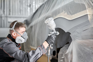 Painting the rear part of the car. Car painter wearing costume and protective gear. Car service...