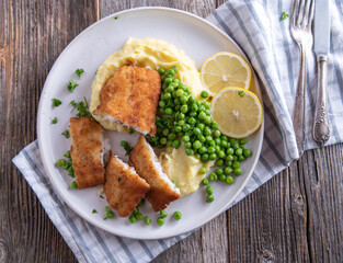 Traditional breaded fish with mashed potatoes and green peas on a plate