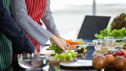 Professional chefs on apron master cooking healthy vegan food by preparing fresh ingredients of tomatoes, onions, and hand mixing with washed organic vegetables on wooden tray