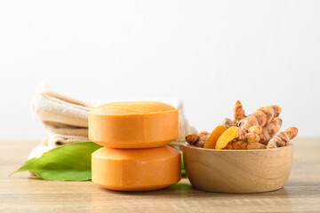 Turmeric soap and fresh turmeric root in a bowl on wooden table with white background, herbal...