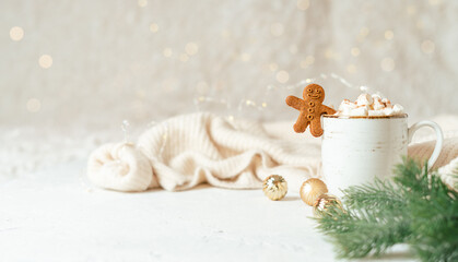 Gingerbread man cookie in cup of hot cocoa or coffee with marshmallow, fir tree, cinnamon and warm cozy sweater. Christmas banner, lights background. Xmas holiday decorations with copy space.