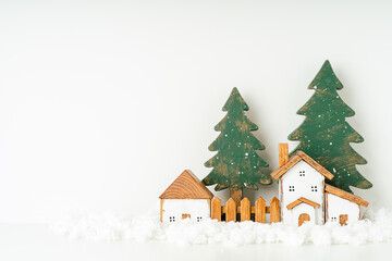 Obraz na płótnie Canvas Happy New Year and Merry Christmas postcard. Festive white background with toy wooden house, snow, rustic christmas tree, village and decoration. Copy space for winter holidays greeting card. 