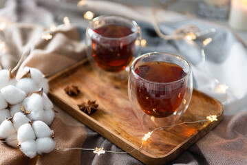 Two cups of black tea with steam on wooden tray on plaid. Hot tea in glass cups with steam in cozy winter composition. Close up. Christmas menu, greeting card. Hygge