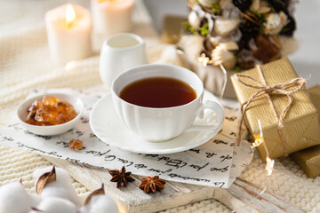 Winter hot tea in a cup in cozy composition. Cups of black tea on wooden tray on knitted plaid with candles, gifts and Christmas tree. Close up, side view. Christmas menu, greeting card, poster