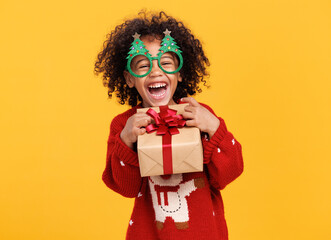 Happy little african american boy wearing funny glasses in form of Christmas trees with xmas gift