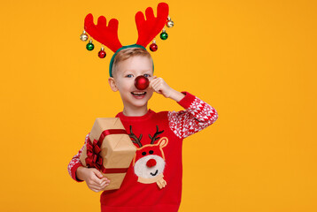 Cheerful little boy with wrapped Christmas gift holding red christmas tree ball in front of his nose