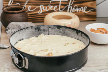 Baking dish with raw apple pie dough stands on kitchen counter next to ingredients and wooden sign Home sweet home