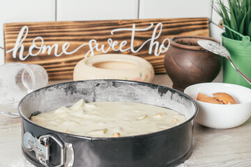 Baking dish with raw apple pie dough stands on kitchen counter next to ingredients and wooden sign Home sweet home