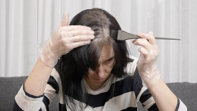 Hair coloring at home. Middle age woman prepares to dye her hair at home, looking at the regrown gray roots of her dark hair