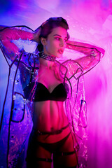 slender woman in a swimsuit and a transparent raincoat in neon light