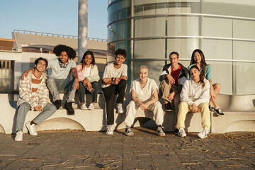 Group of diverse teenager university student friends sitting on modern urban city area at sunset...