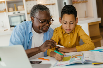 Grandfather tutoring his grandson at home. The child is patiently listening and learning while...