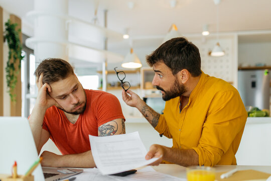 A Gay Couple Paying Bills Online. They Are Talking About How Much They Spent On Unnecessary Things.