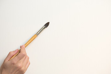 The artist's hand holds an artistic brush against a white sheet of paper