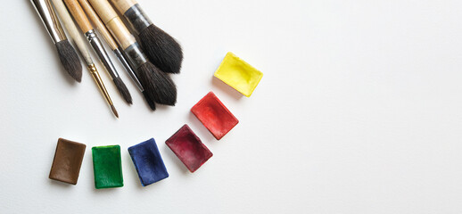 Art brushes with wooden handles and containers of watercolor paints on a white background