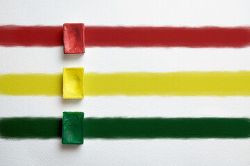 Red, yellow and green container of watercolor paint on a background of multicolored stripes