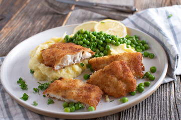 Breaded fish with mashed potatoes and green peas on a plate