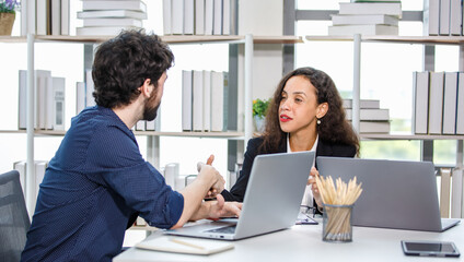 Caucasian bearded businessman trainee working  with African American businesswoman manager trainer in formal suit sitting teaching coaching at working desk