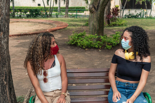 Two friends with protective mask sitting on a park bench