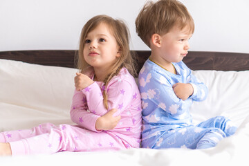 Two Preschool Toddler Children Siblings Boy And Girl Portray Resentful Upset In Pink Blue Pajamas On White Bed. Little Baby Twins Have Fun. Happy Kids On Quarantine At Home. Friendship, Family Concept