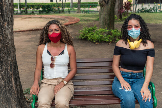 Two friends with protective mask sitting on a park bench