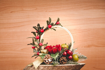 Christmas wreath of leaves and berries resting on bark, with pine cones, fruits on wooden background