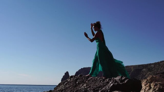 Side view a Young beautiful sensual woman with black hair in a long mint dress posing on a beach with calm sea bokeh lights on sunny day. Girl on the nature on blue sky background. Fashion photo