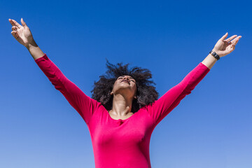 Afro woman raises her arms with an air of freedom on a sunny day